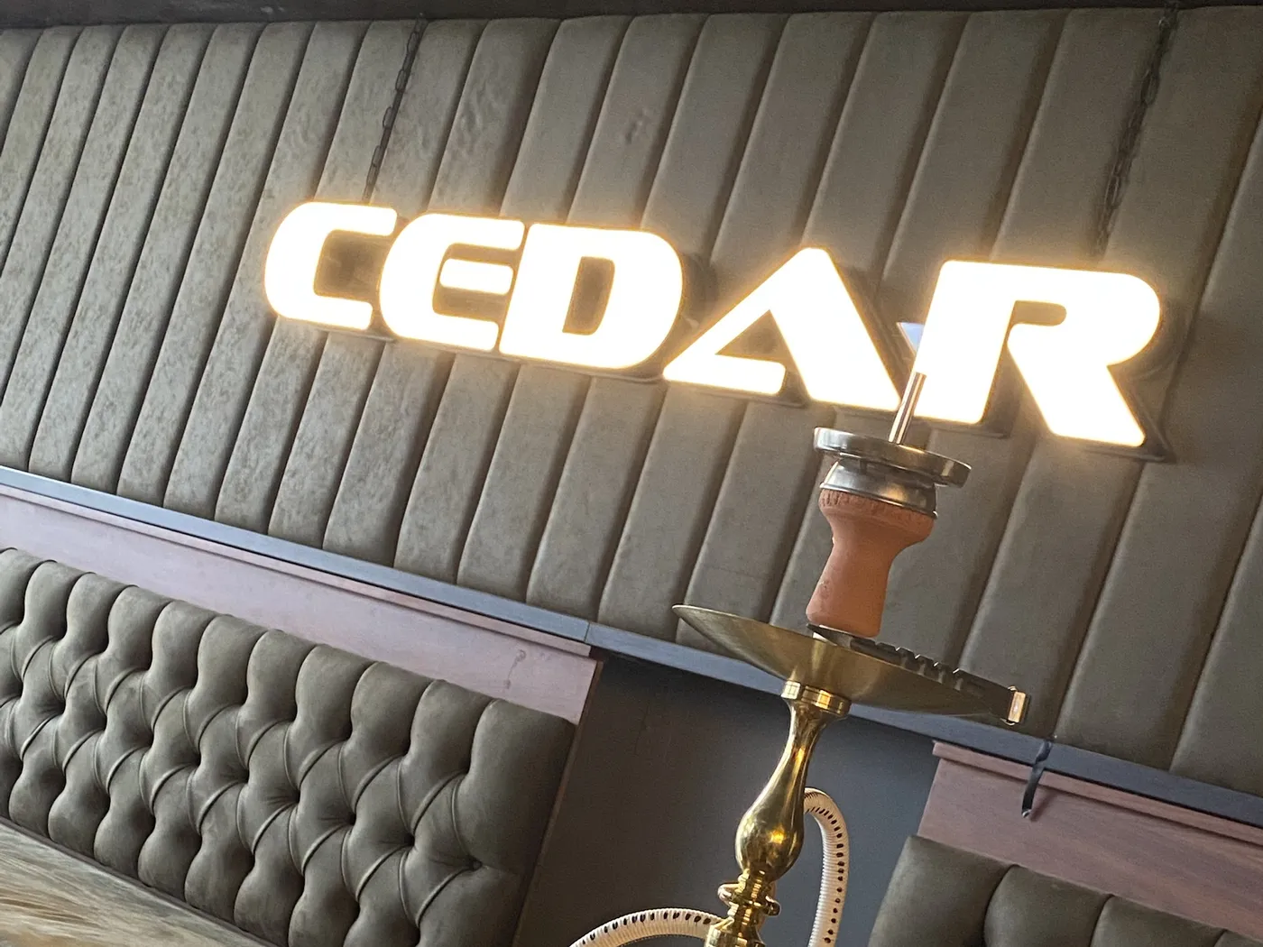 A gold Cedar shisha in front of the lit CEDAR sign